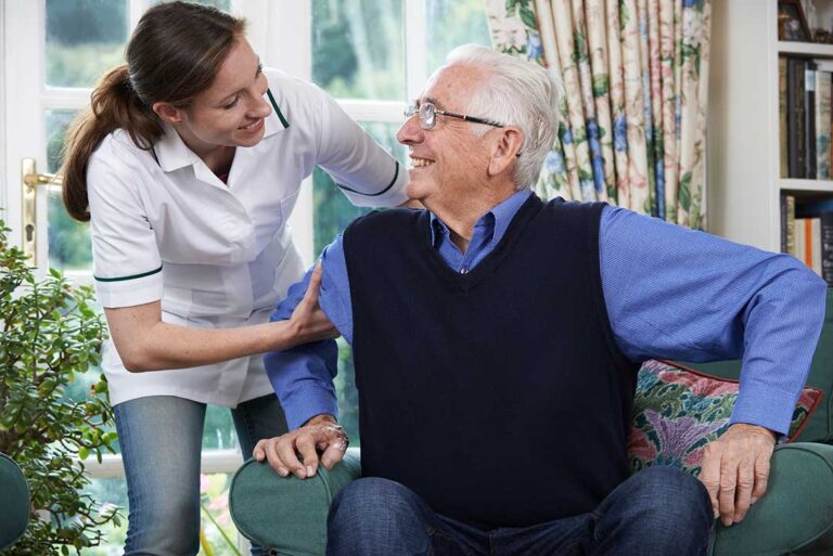 Two older adults laughing together while playing cards in a sunny common room.